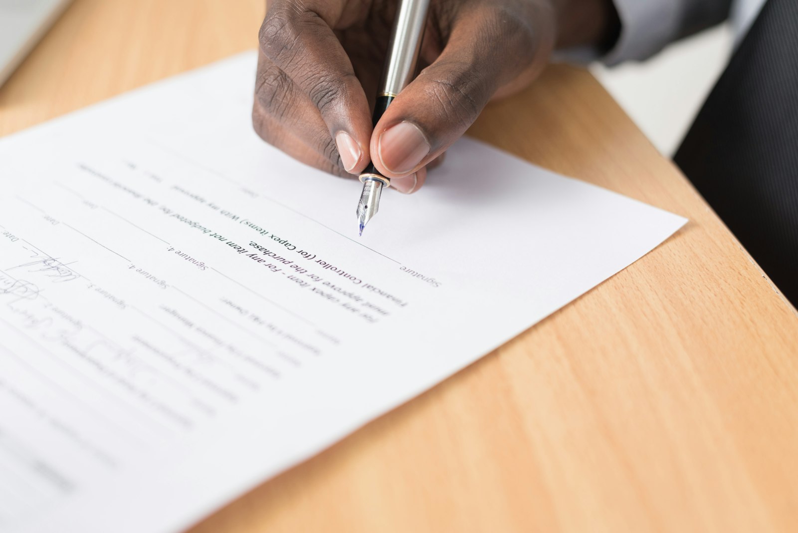A hand signing a printed document with a pen